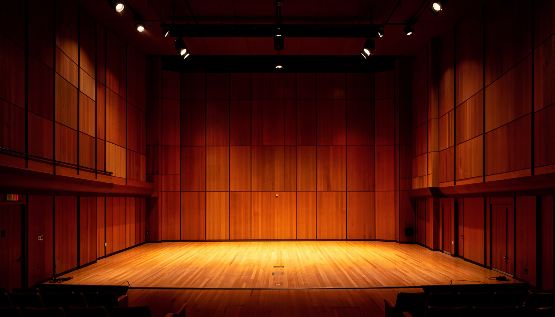 A symmetrical concert hall stage with warm wood paneling and dark amber lighting conveying a calm and focused atmosphere